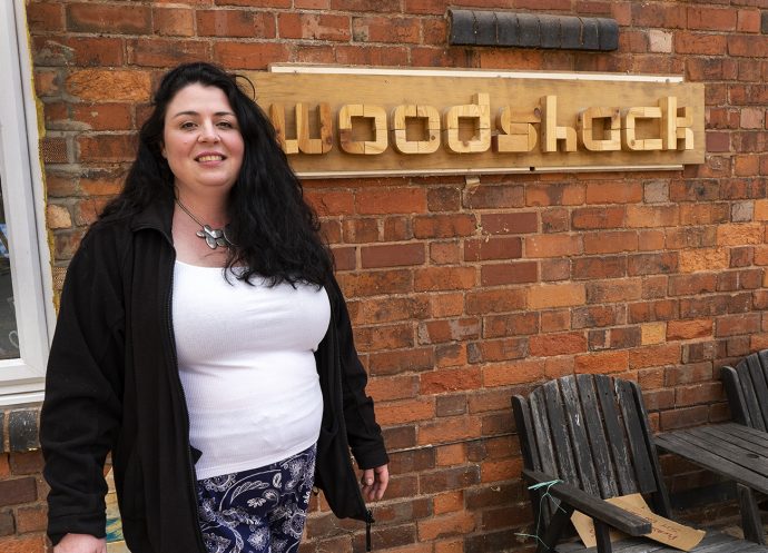 Business owner standing next to sign bearing its name.