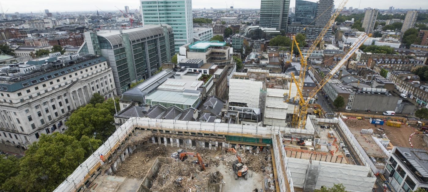 Aerial view of a tower block being demolished from the top down.