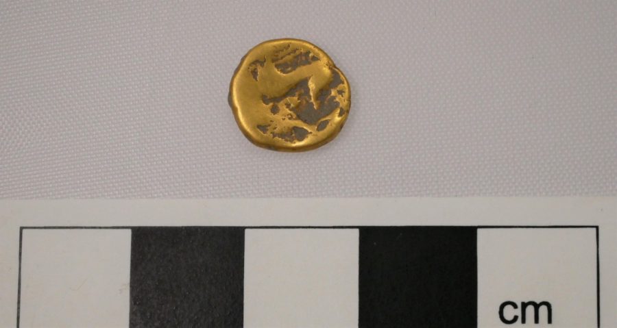 A gold coin, uninscribed, next to an ruler showing its size as about 1cm.