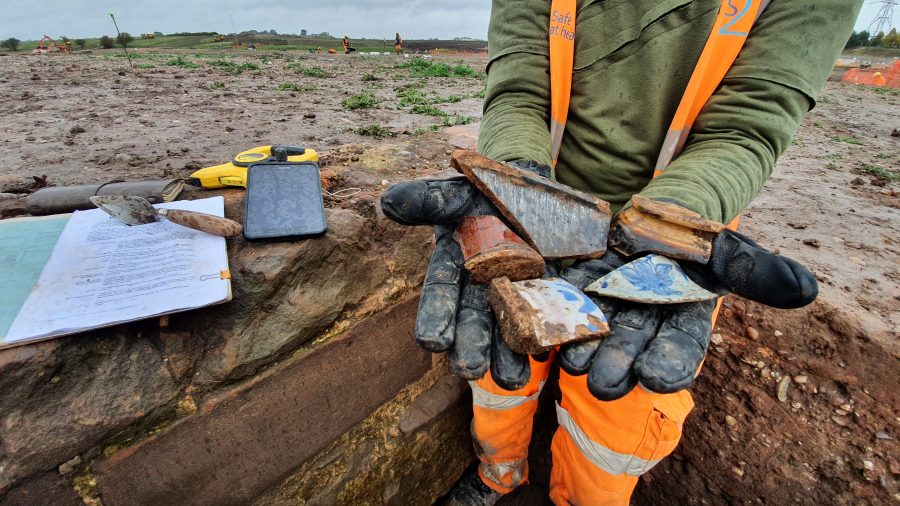A Wessex Archaeologist presents some post medieval pottery sherds from the site of Coleshill Medieval Manor. In the photo can be seen a digital recording tablet, a trowel and an archaeologists tools.