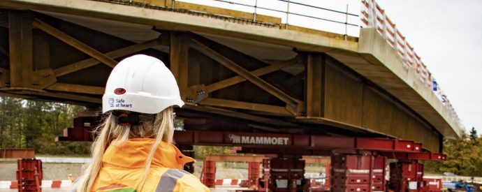 Woman facing away from camera with white hard hat on and orange PPE looking over a bridge being moved